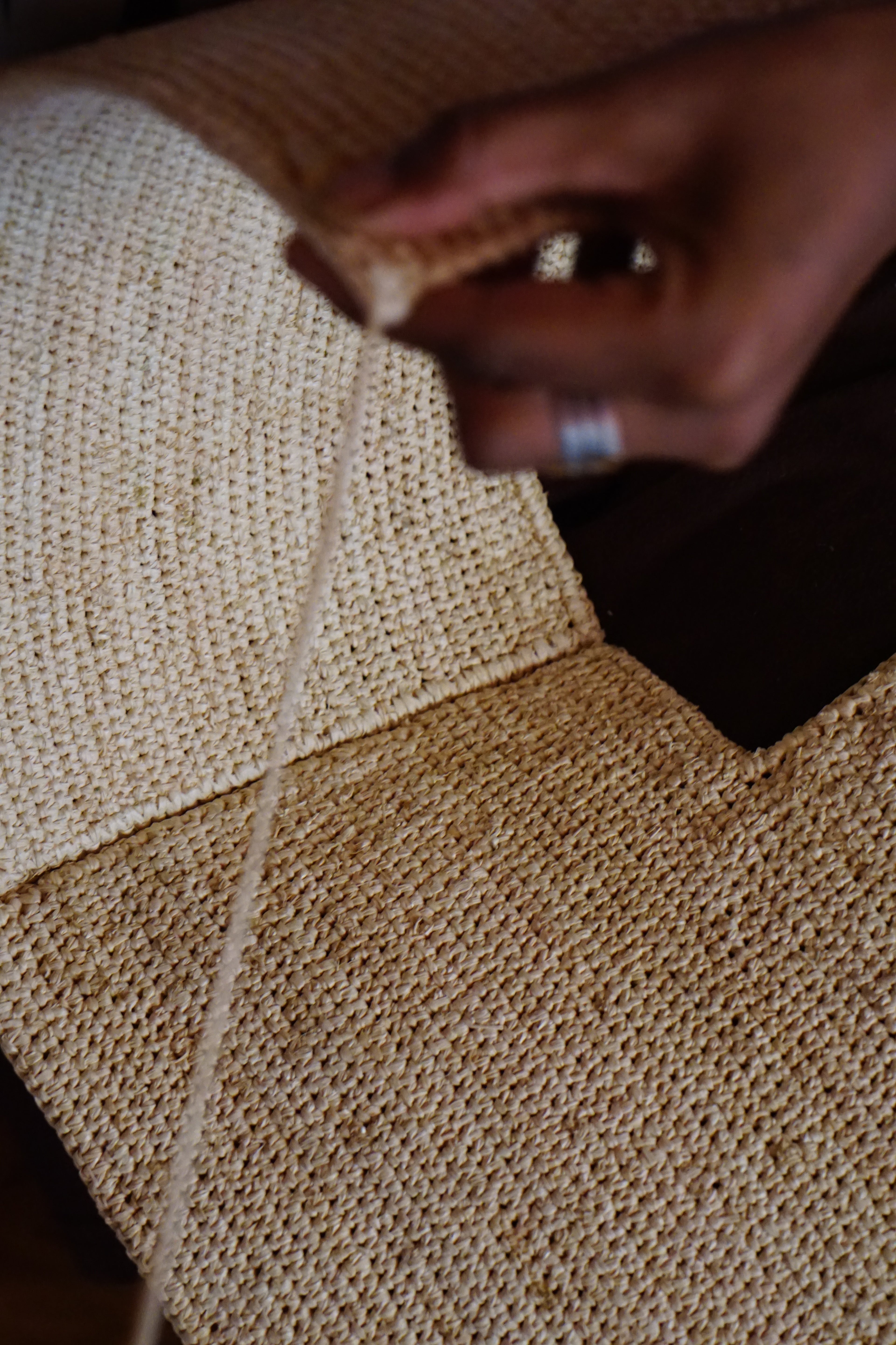 Zoom sur des mains crochetant un sac en raphia, mettant en valeur les détails du tissage fait-main et la texture naturelle de la fibre.