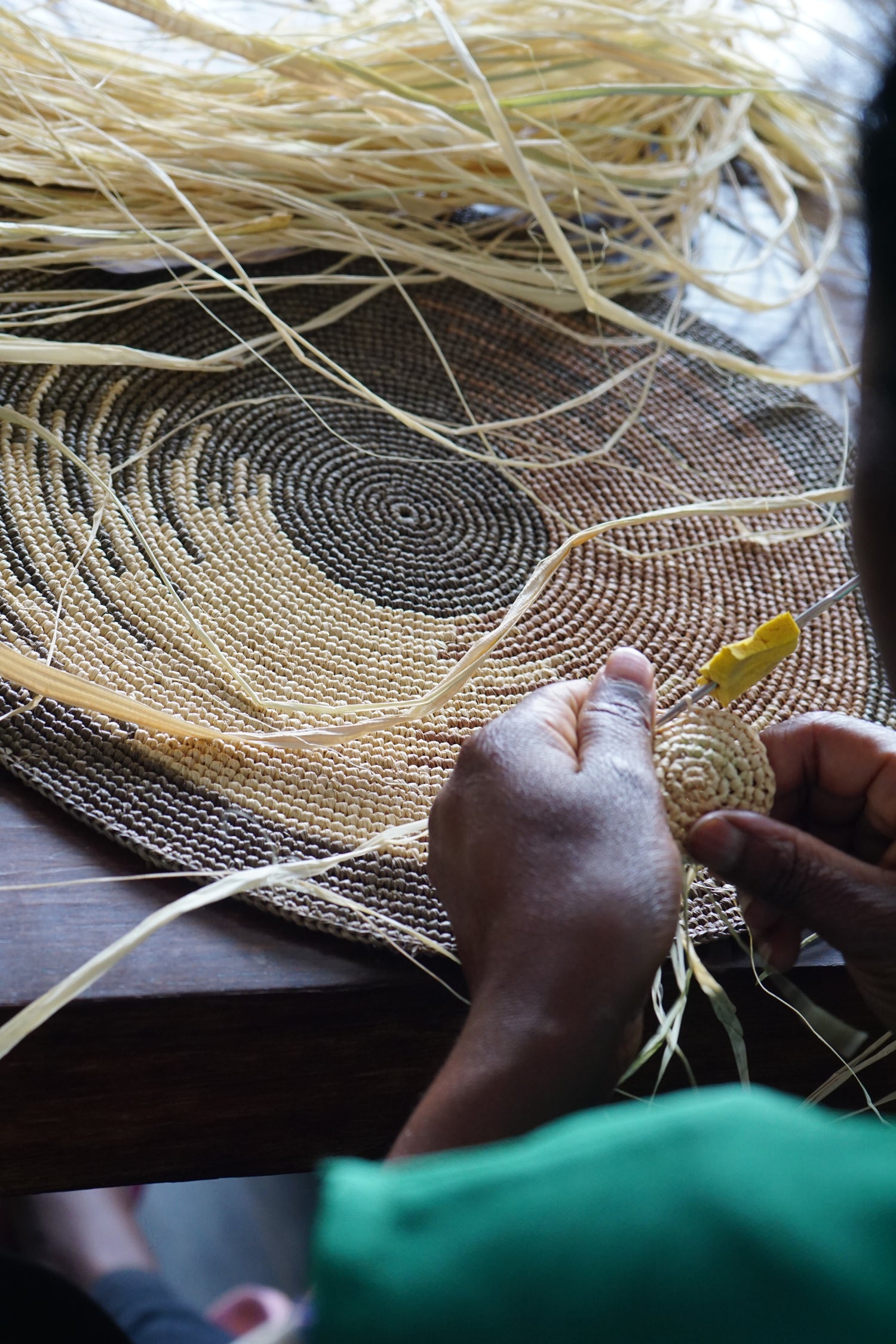 Zoom sur des mains crochetant un set de table en raphia, mettant en valeur les détails du tissage fait-main et la texture naturelle de la fibre.