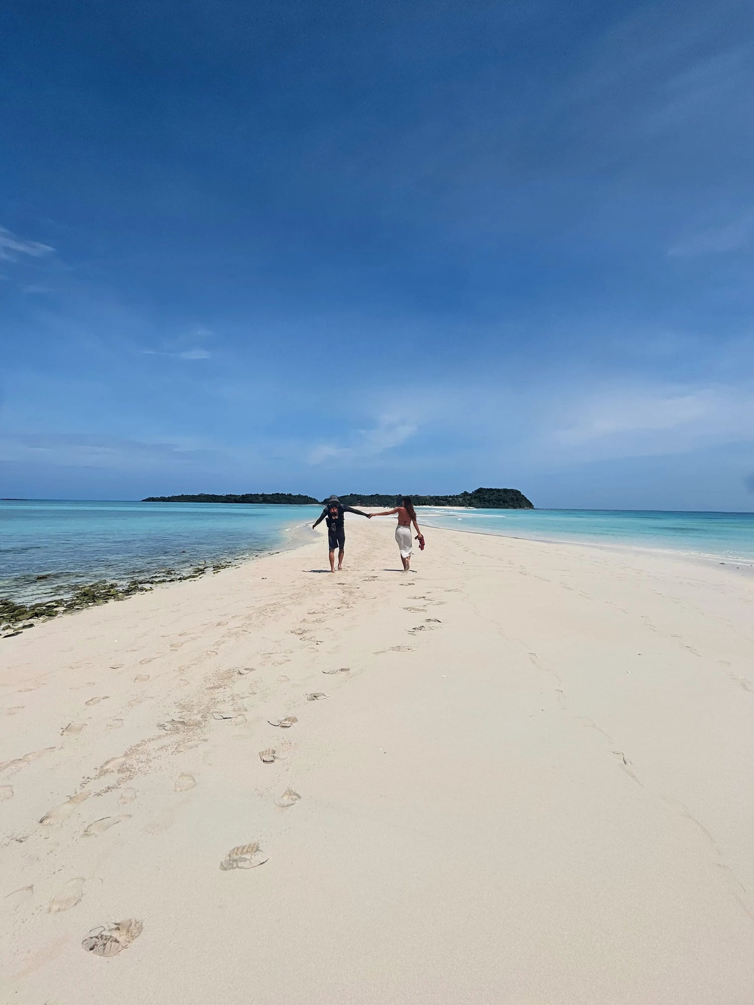 Un jeune couple marchant main dans la main sur le sable blanc de l'île Nosy Iranja, à Madagascar - OQENA