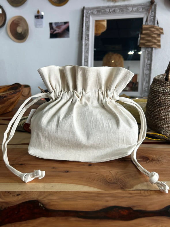 Petit pochon en coton crème sur table en bois, décor artisanat avec miroir et objets tissés en arrière-plan