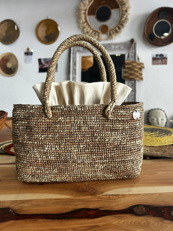 Sac en raphia tressé avec anses rondes et doublure crème sur table en bois
