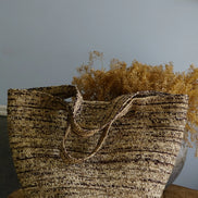 Sac en paille tressée brun naturel avec anses sur table ronde en osier et décor de plante sèche