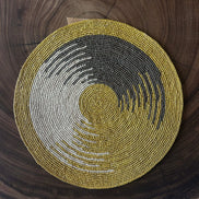 Set de table rond en raphia tressé avec motifs jaunes, gris et blancs sur table en bois